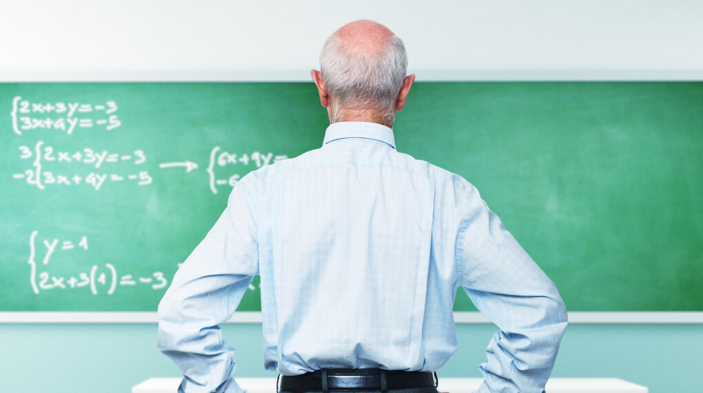 Older teacher standing in front of a chalk board