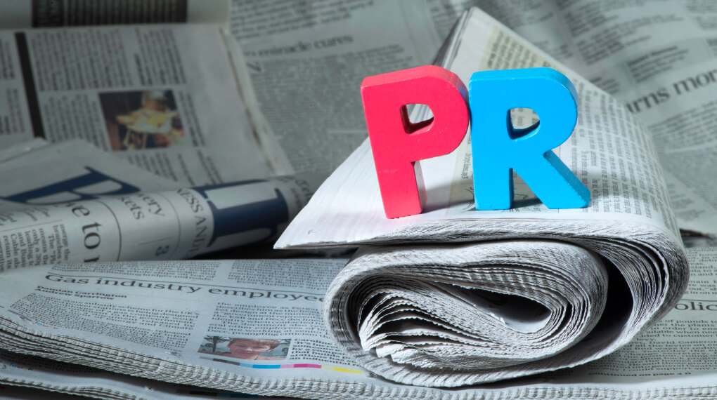 Woodblock letters spelling PR sitting atop a stack of newspapers